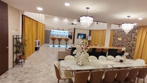 Un amplio comedor con una mesa y sillas de mármol, una zona de bar al fondo y cortinas amarillas.