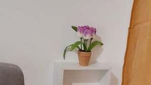 A corner of a room with a grey sofa, a white shelf with a potted plant, and a brown curtain. - Delizioso Appartamento, Totalmente Ristrutturato 5 Posti Letto (Palermo)