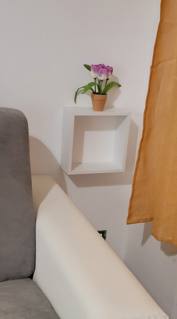 En hörna i ett rum med en grå soffa, en vit hylla med en krukväxt och en brun gardin.