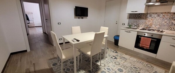 A compact kitchen with a dining table, chairs, a TV mounted on the wall, and a patterned floor. - Delizioso Appartamento, Totalmente Ristrutturato 5 Posti Letto (Palermo)