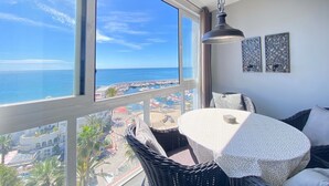 A balcony with a view of the sea, a round table with a white tablecloth, wicker chairs, and two wall-mounted decorative items. - Valdecantos Marina . (Marbella)