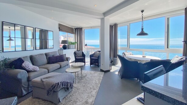 A modern living room with a sofa, armchairs, and a dining area. Large windows offer a view of the ocean. - Valdecantos Marina . (Marbella)