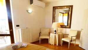 A hotel room with a bed, two chairs, a small table with a lamp, a mirror, and a radiator. - Private Villa with hot tub, WIFI, private pool, A/C, TV, terrace, panoramic view, close to Sirmione (Polpenazze Del Garda)