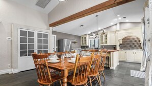 Una cocina amplia con comedor, que presenta un gran mesa de madera, armarios blancos y un refrigerador moderno de acero inoxidable.