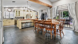 Una cocina amplia con armarios de madera, una mesa de comedor con sillas y un gran ventanal con cortinas.