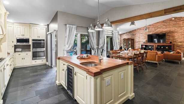 Una cocina amplia con armarios blancos, una isla central y una pared decorada con ladrillo.