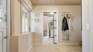 A hallway with a tiled floor, a coat rack with hats, and a door with a window.