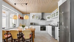 A modern kitchen with white cabinets, a stainless steel refrigerator, and a dining area with wicker chairs and a wooden table.