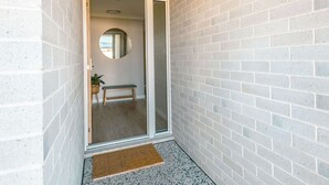 A narrow hallway with a white brick wall, a wooden bench, a small round mirror, and a doormat.