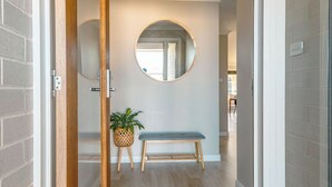 A hallway with a wooden bench, a round mirror on the wall, and a potted plant.