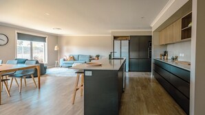 A modern kitchen with a central island, a dining area with wooden furniture, and a living space with a sofa and a coffee table.