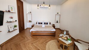 Een moderne slaapkamer met een houten bed, nachtkastjes, een televisie en een klein rond tafeltje met een stoel.