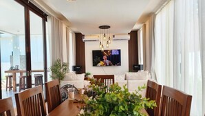 Een ruime woonkamer met een grote houten eettafel, witte banken en een flatscreen televisie aan de muur.