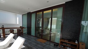 Een modern interieur met een glazen deur naar een balkon, een zithoek met lounge fauteuils en een schoenenrek.