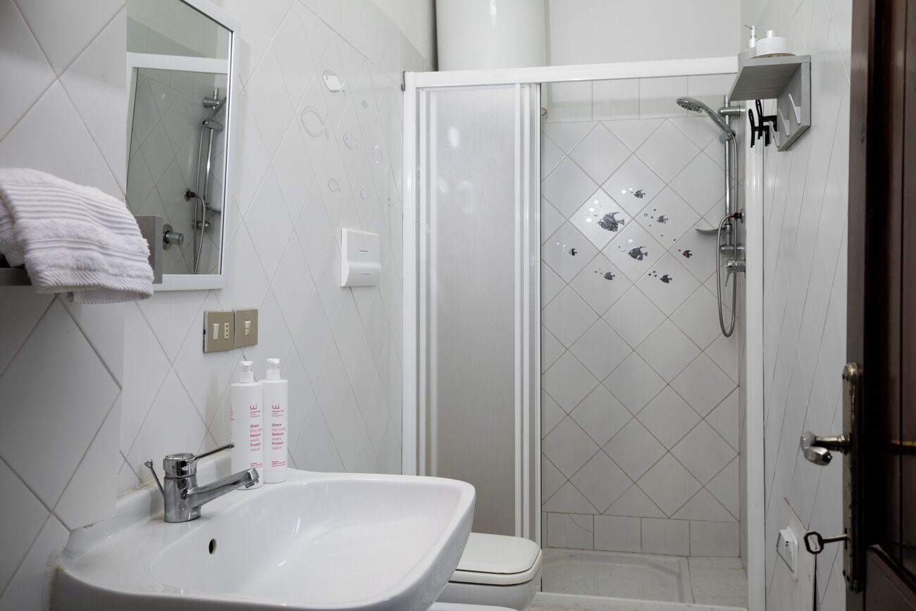 Un baño con lavamanos blanco, espejo, inodoro y cabina de ducha con mampara de vidrio.