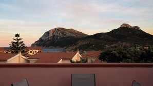 Un balcon avec deux chaises, donnant sur une zone côtière avec des bâtiments et une montagne.