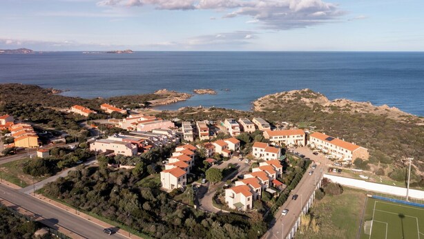 Vue aérienne d’une zone résidentielle côtière, avec des maisons, une route et une vue dégagée sur la mer.