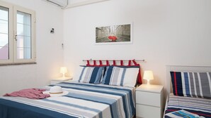 Ein Hotelzimmer mit zwei Betten, gestreifter Bettwäsche, einem rot-weiß gestreiften Kopfteil, einem Fenster und einem Wandbild.