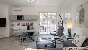 Un salon moderne avec une table basse en verre, un canapé agrémenté de coussins à motifs, un fauteuil suspendu et un coin repas comprenant une table et des chaises.
