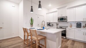 Uma cozinha moderna com armários brancos, uma ilha central e um espaço de jantar com duas cadeiras.