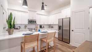 Uma cozinha moderna com armários brancos, eletrodomésticos de aço inoxidável e uma ilha central com duas cadeiras.