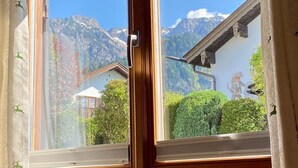 Habitació amb una finestra gran que dona a un paisatge de muntanya, una porta de fusta i una paret blanca amb un dibuix decoratiu.