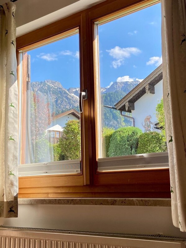 Una habitación con un amplio ventanal que da a un paisaje montañoso, una puerta de madera y una pared blanca con un diseño decorativo.