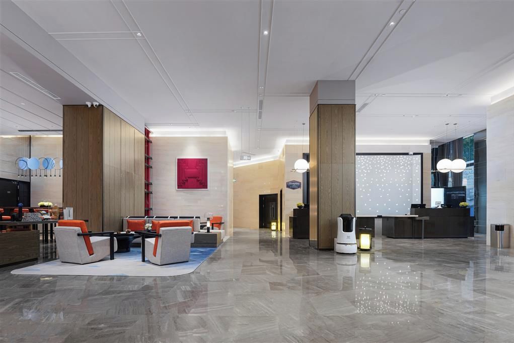 Un moderno vestíbulo de hotel con una recepción, zona de estar y una gran pared con luces decorativas.