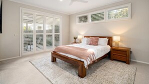 Ein Schlafzimmer mit einem Holzbett, zwei Nachttischen mit Lampen, einem Deckenventilator und großen Fenstern mit Jalousien.