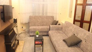 A living room with a sofa, a small table with a plant, a television, and a piano. - mater dei <br>suite near royal Liverpool hospital (Liverpool)