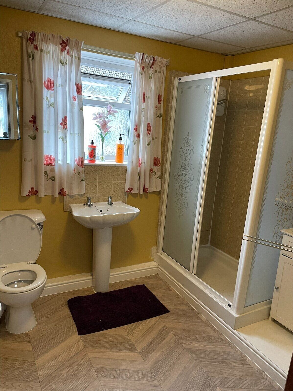 A bathroom with a toilet, sink, shower, and floral curtains.