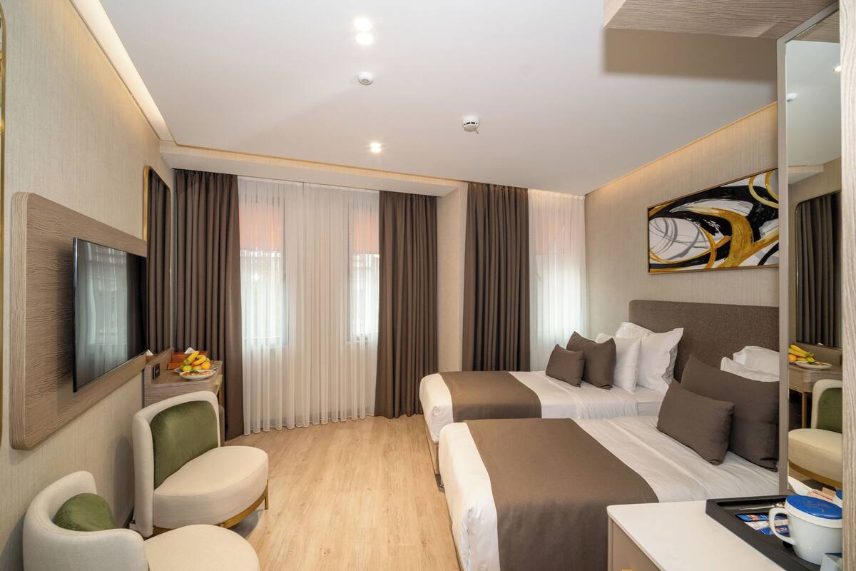 Une chambre d’hôtel moderne équipée de deux lits, d’un téléviseur à écran plat, d’un bureau avec un panier de fruits et d’un grand miroir.