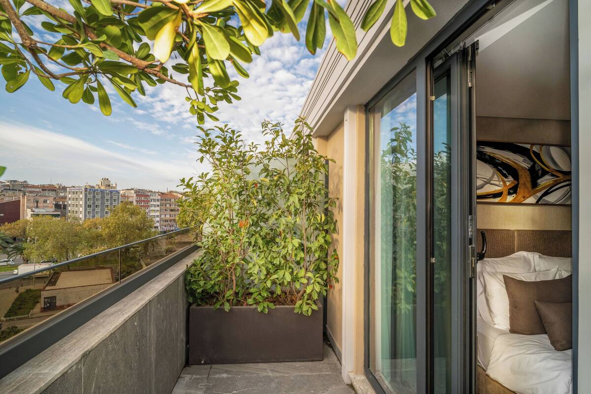 Un balcon avec vue sur la ville, un lit avec des oreillers et un jardinière agrémentée de plantes vertes.