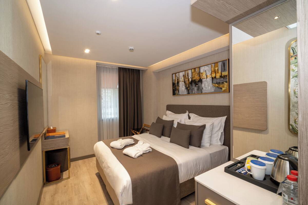 Une chambre d’hôtel moderne avec un grand lit, un téléviseur à écran plat, une table de chevet avec une lampe et un tableau au mur.