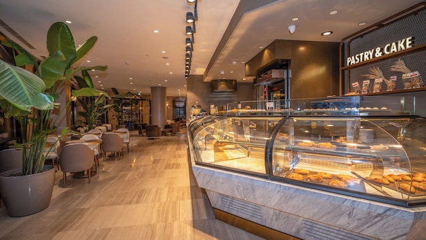 A modern hotel lobby with a pastry and cake display, seating area, and potted plants. - Rayelin Hotel Old Town  (Istanbul)