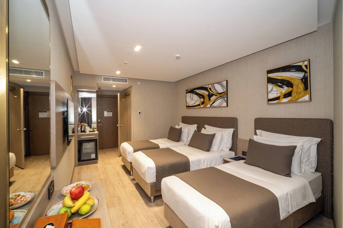 Une chambre d’hôtel avec deux lits, une petite kitchenette, un miroir et des œuvres d’art accrochées aux murs.