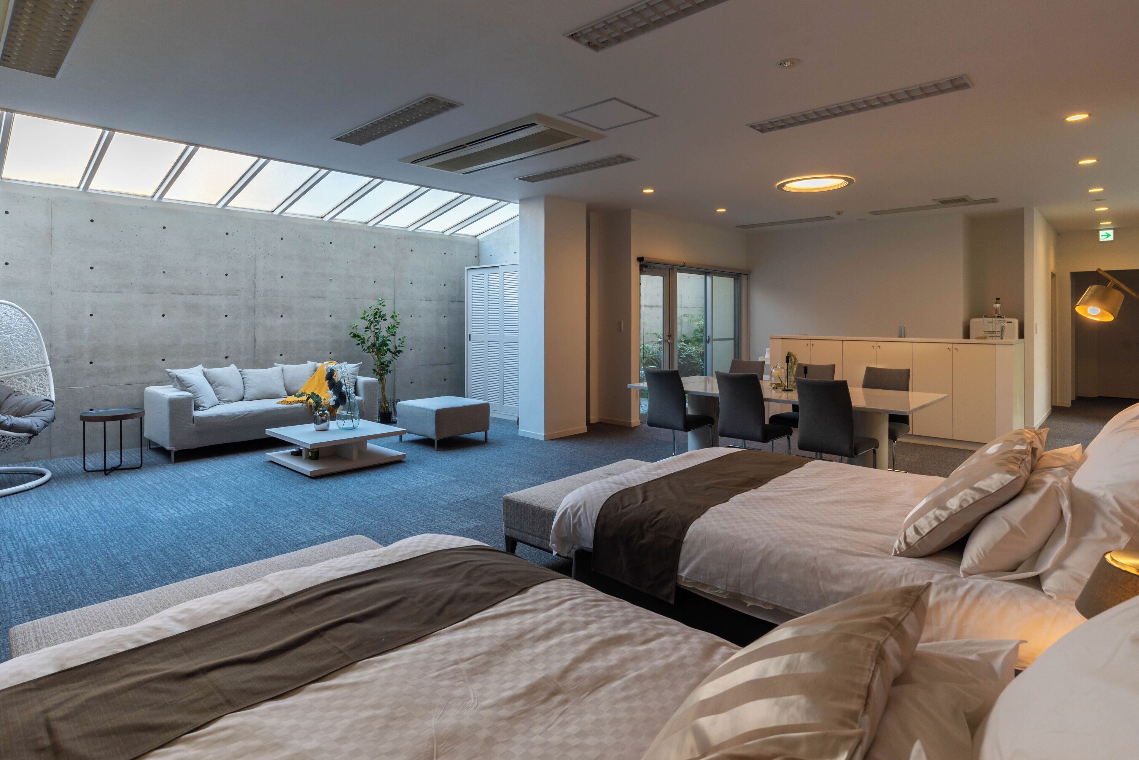 Ein modernes Hotelzimmer mit einem großen Bett, einer Sitzecke, einem kleinen Tisch und einem Schreibtisch. Ein großes Fenster sorgt für natürliches Licht und bietet einen Blick ins Freie.