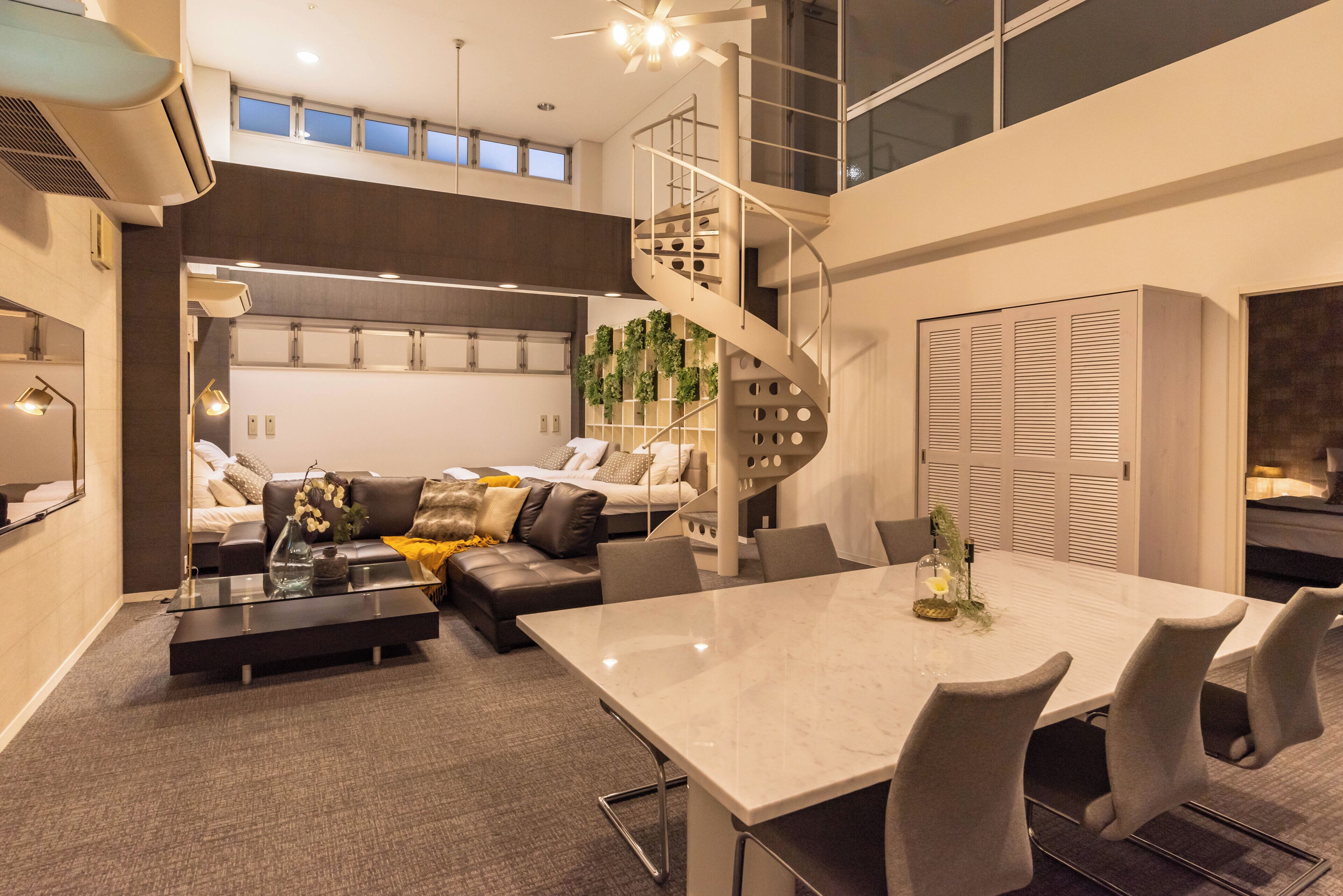 Een moderne woonkamer met een glazen salontafel, een bank, een eettafel met stoelen, een wenteltrap en uitzicht op de stad door grote ramen.