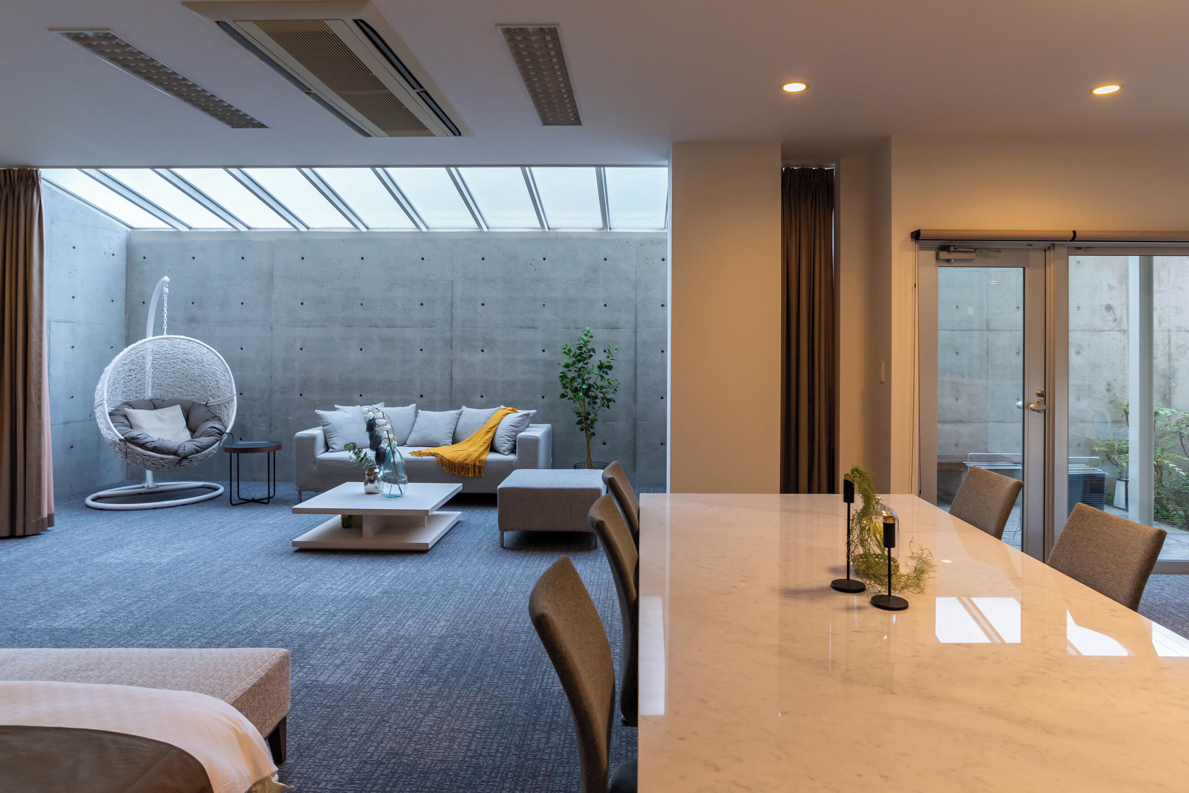 Una habitación de hotel moderna con una gran mesa de comedor, asientos cómodos, una silla colgante y vistas amplias a través de ventanas grandes.