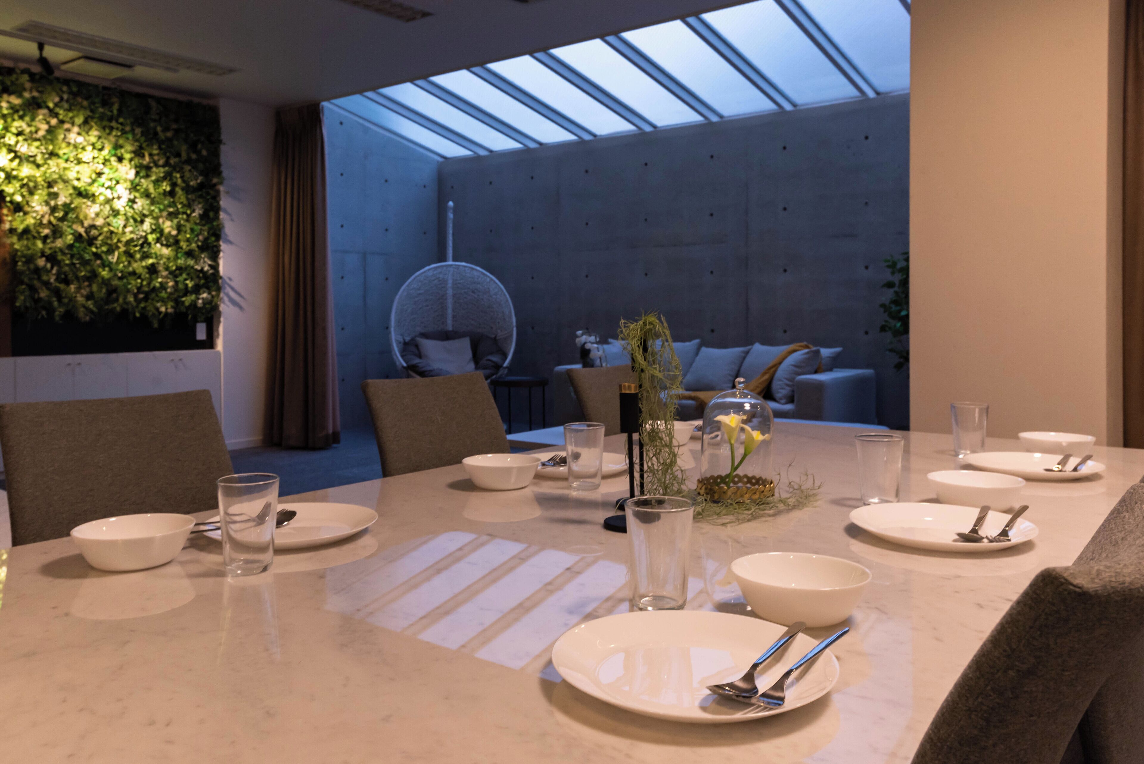 Un comedor moderno con una mesa larga dispuesta para una comida, un sillón colgante y una pared cubierta de plantas.