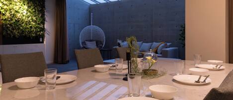Un comedor moderno con una mesa larga dispuesta para una comida, un sillón colgante y una pared cubierta de plantas.