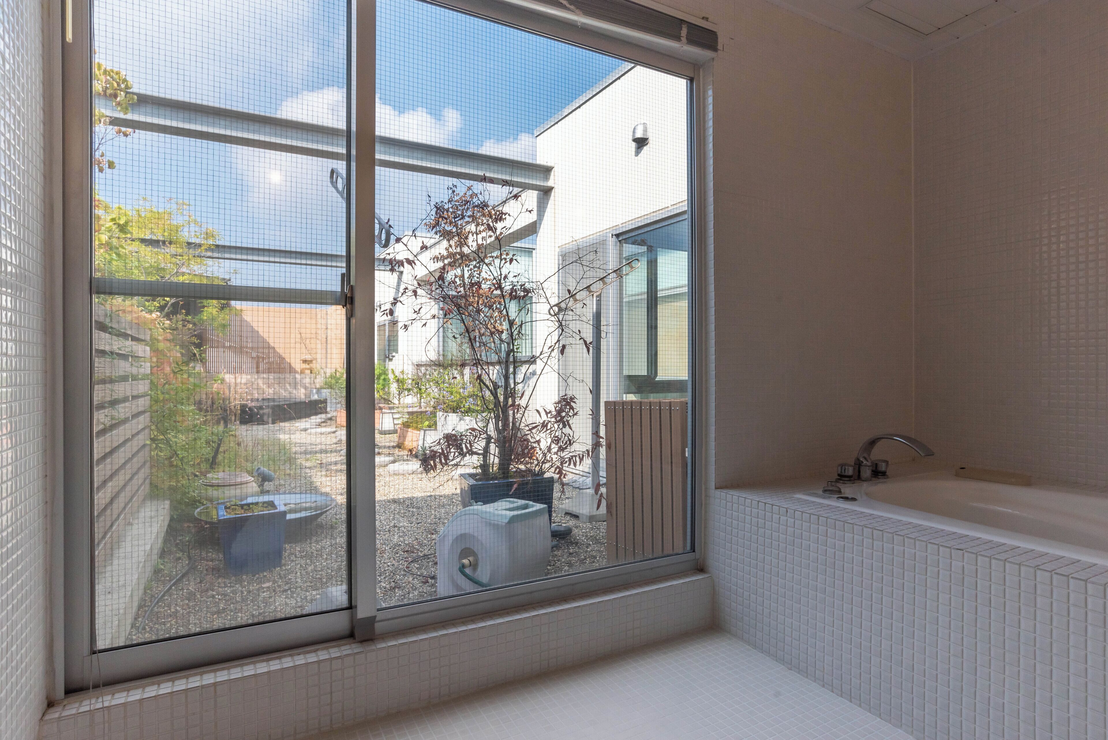 Een badkamer met een groot raam, een bad en uitzicht op een tuin.