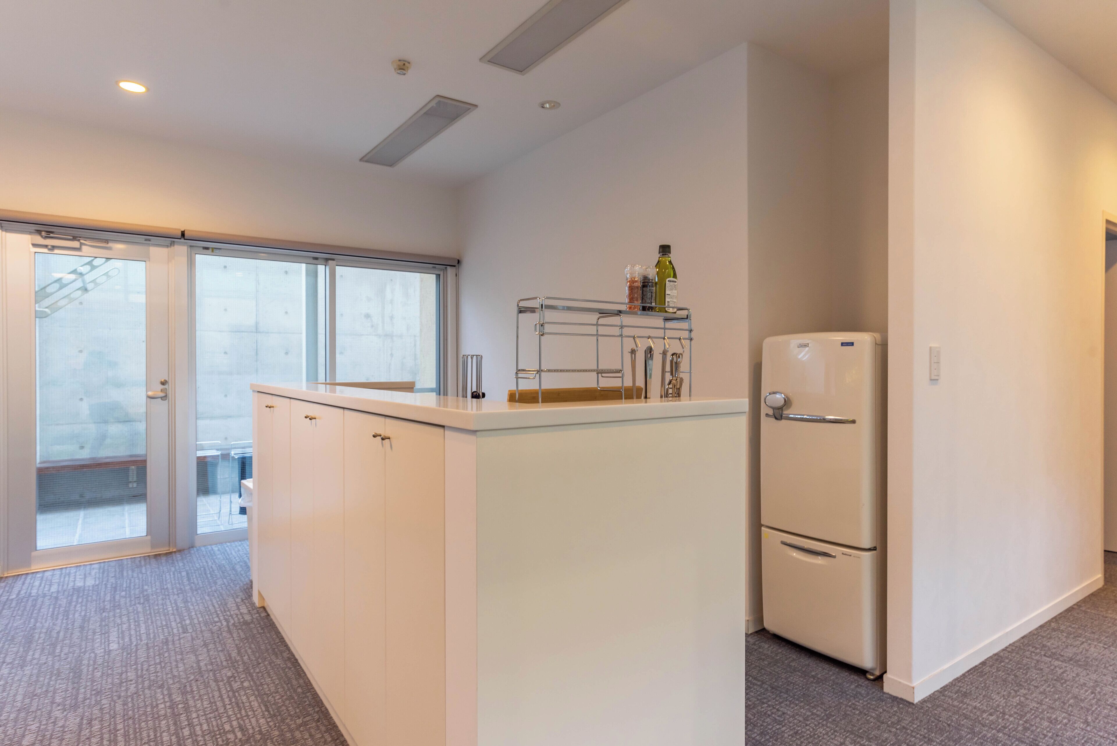A modern kitchen with white cabinetry, a built-in refrigerator, and a small countertop with a bottle of olive oil.