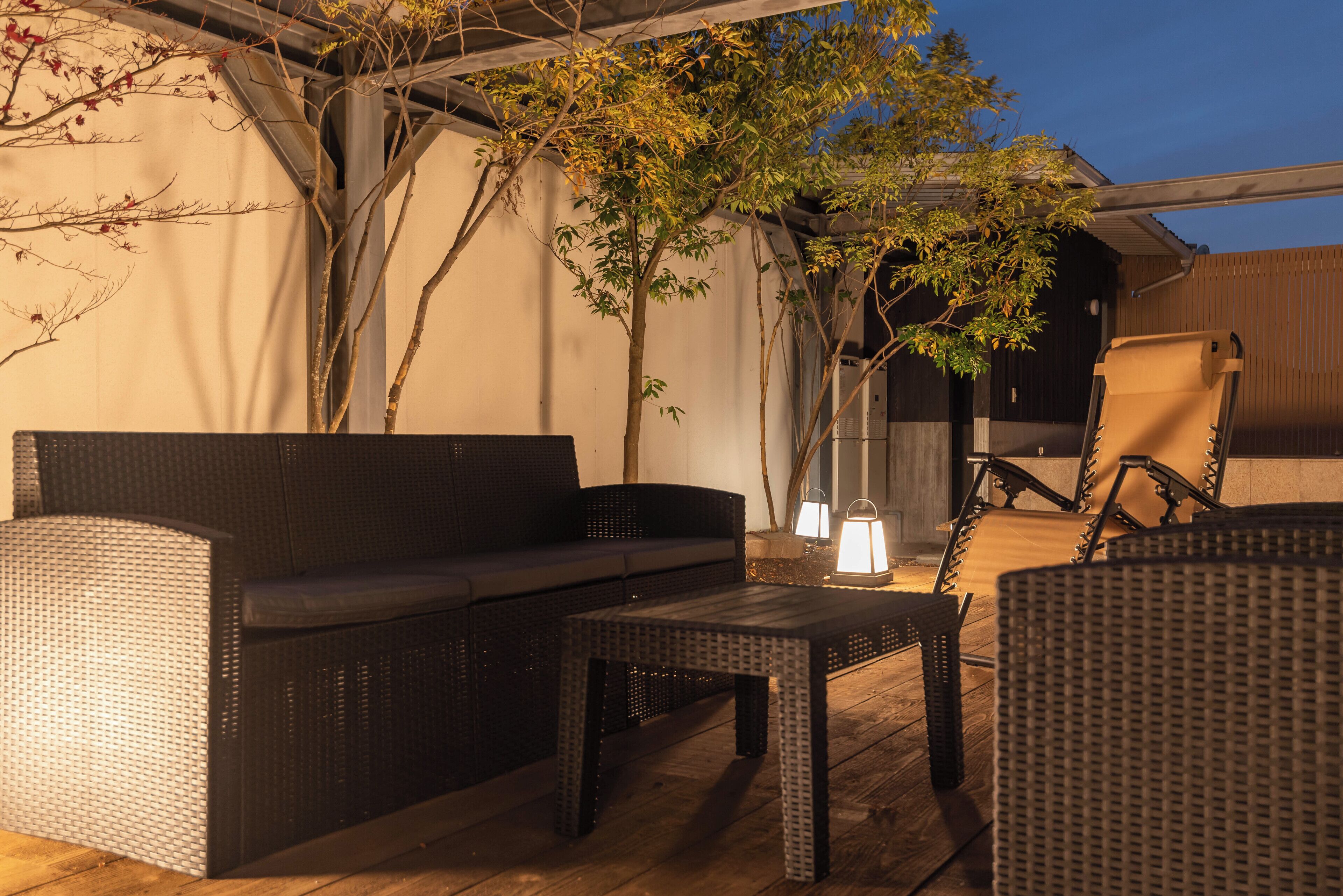 Une terrasse extérieure aménagée avec des meubles en osier, notamment un canapé et des fauteuils, ainsi qu’une table.