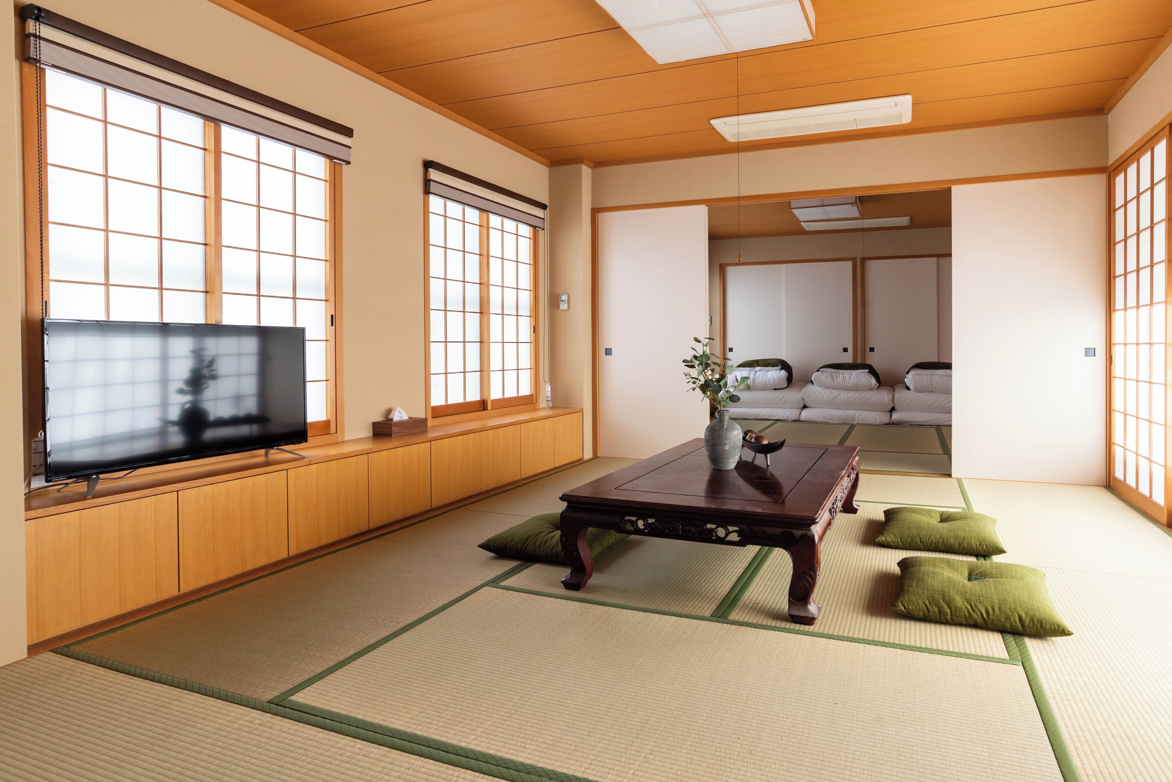 A traditional Japanese-style room with tatami flooring, a low wooden table, a television, and sliding doors leading to a sleeping area with futons.