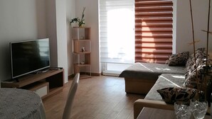 A modern living room with a flat-screen TV, a dining table with chairs, a sofa, and a window with blinds. - Impeccable 2-bed Apartment in Rab (Rab)