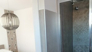 A modern bathroom with a glass shower enclosure, a bed with a white mattress and beige headboard, and a decorative wall with a floral pattern. - Impeccable 2-bed Apartment in Rab (Rab)