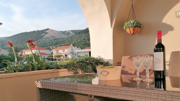 An outdoor patio with wicker furniture, a table, and a bottle of wine. - Impeccable 2-bed Apartment in Rab (Rab)