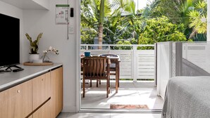 A modern kitchen with a TV, wooden cabinets, and a dining area with a table and chairs. - Belongil Beach Pad Byron Bay (Byron Bay)