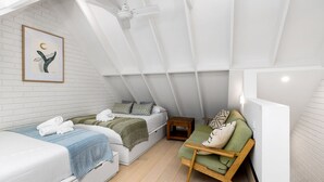 A modern loft bedroom with a sloped ceiling, a bed, a chair, and a small table. - Belongil Beach Pad Byron Bay (Byron Bay)